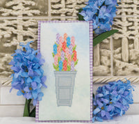 A framed cross-stitch artwork depicting colorful tulips in a gray pot, styled with blue hyacinth flowers against a textured beige tile background.