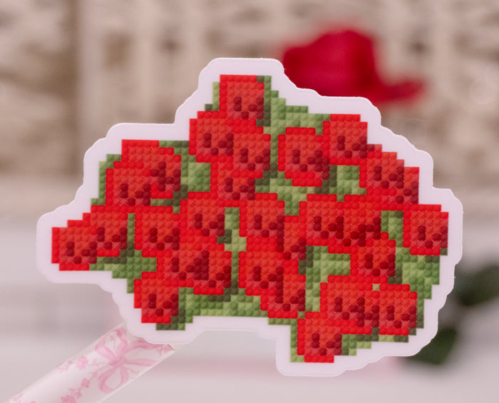 A die-cut sticker featuring a pixelated, diamond-paint style design of a bouquet of red roses with green leaves, shown on a white stick with a blurred background.