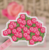 A die-cut sticker featuring a pixel-art style pink rose bouquet with green leaves, shown on a pink ribbon against a softly blurred background.