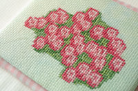 A close-up of a hand-embroidered floral design featuring pink roses with green leaves on a pale mint green fabric background.