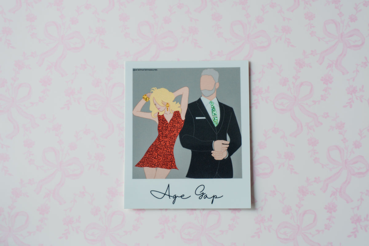 A square glitter polaroid sticker with a white border, featuring a stylized illustration of a blonde woman in a red dress next to a man in a black suit with a green patterned tie. The text 'Age Gap' is written in black script at the bottom.