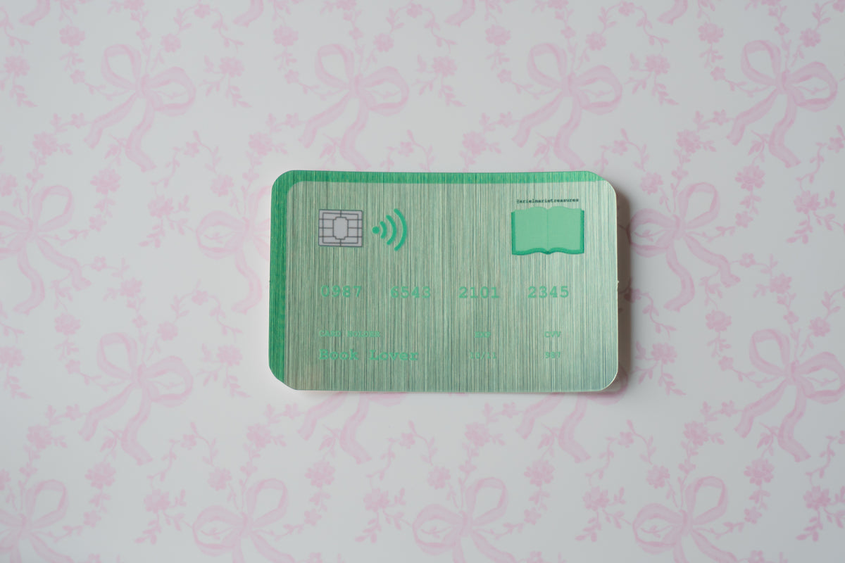 A green metallic credit card sticker with a chip and wireless icon, placed on a light pink patterned background.