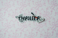 A die-cut sticker with the text 'In my THRILLER era!' and small illustrations, placed on a light pink floral wallpaper background.