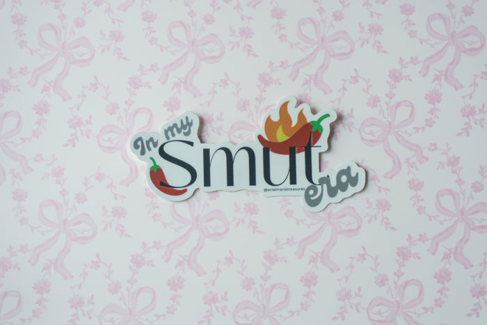 A die-cut sticker with the text 'In my Smut era' and chili pepper illustrations, displayed on a light pink patterned background.