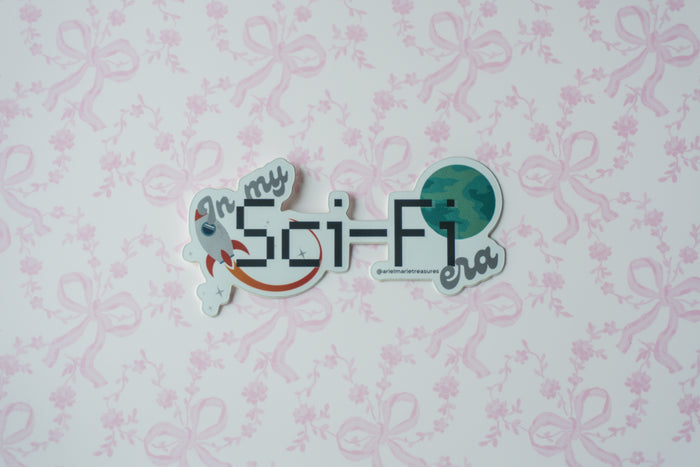 A die-cut sticker with the text 'In my Sci-Fi era' and space-themed illustrations, placed on a light pink floral bow patterned background.