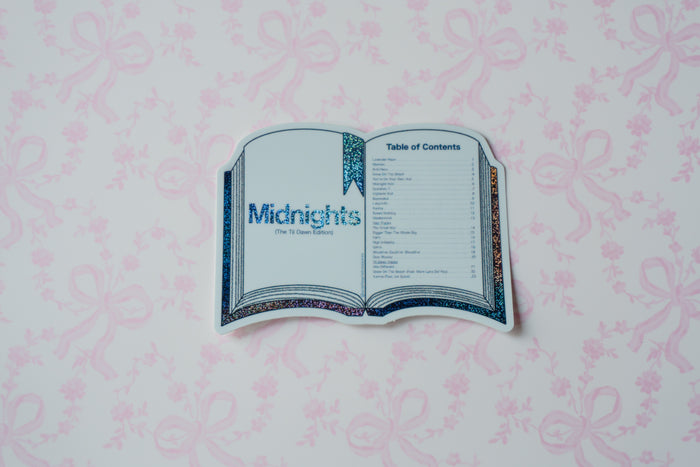 A die-cut sticker shaped like an open book, featuring the title 'Midnights' and a table of contents, displayed on a light pink patterned background.
