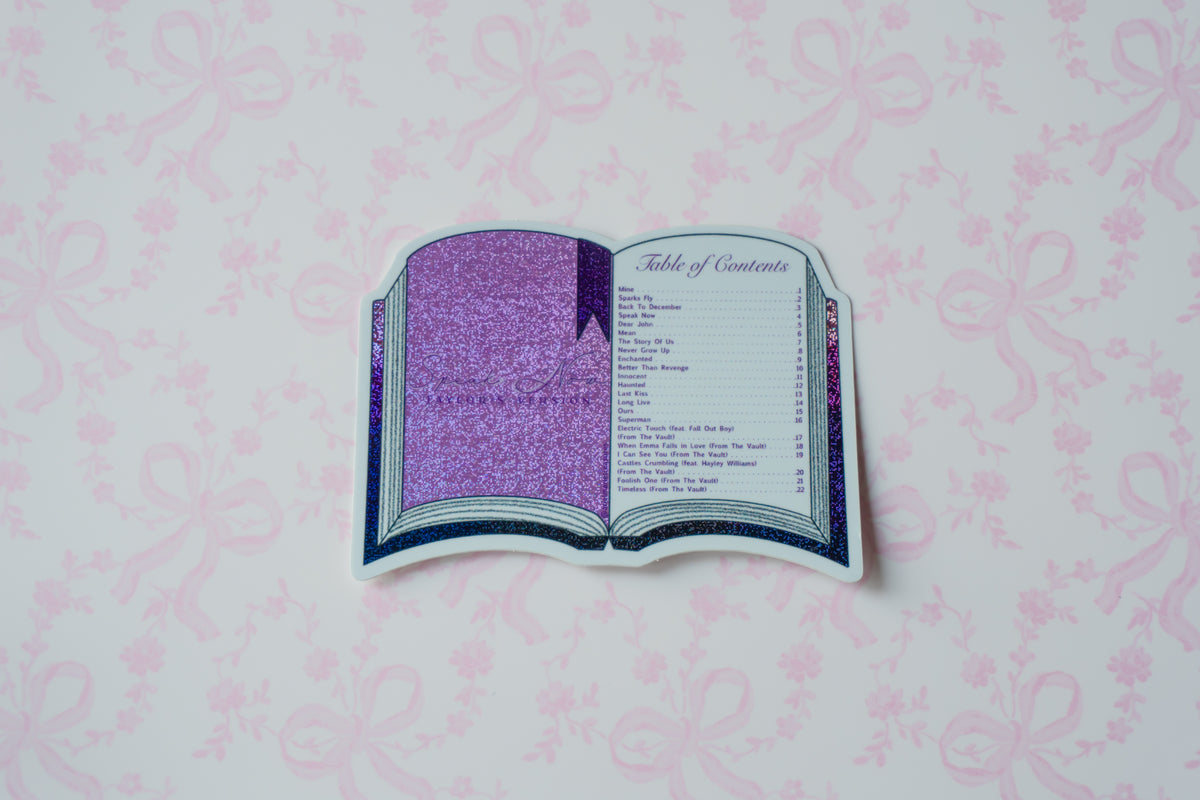 A die-cut sticker shaped like an open book displaying a purple glittery table of contents, placed on a light pink patterned background.