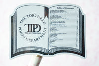 A novelty book-shaped sign or prop featuring the title 'The Tortured Poets Anthology' with a table of contents printed on the right page, mounted on a white handle against a plain white background.