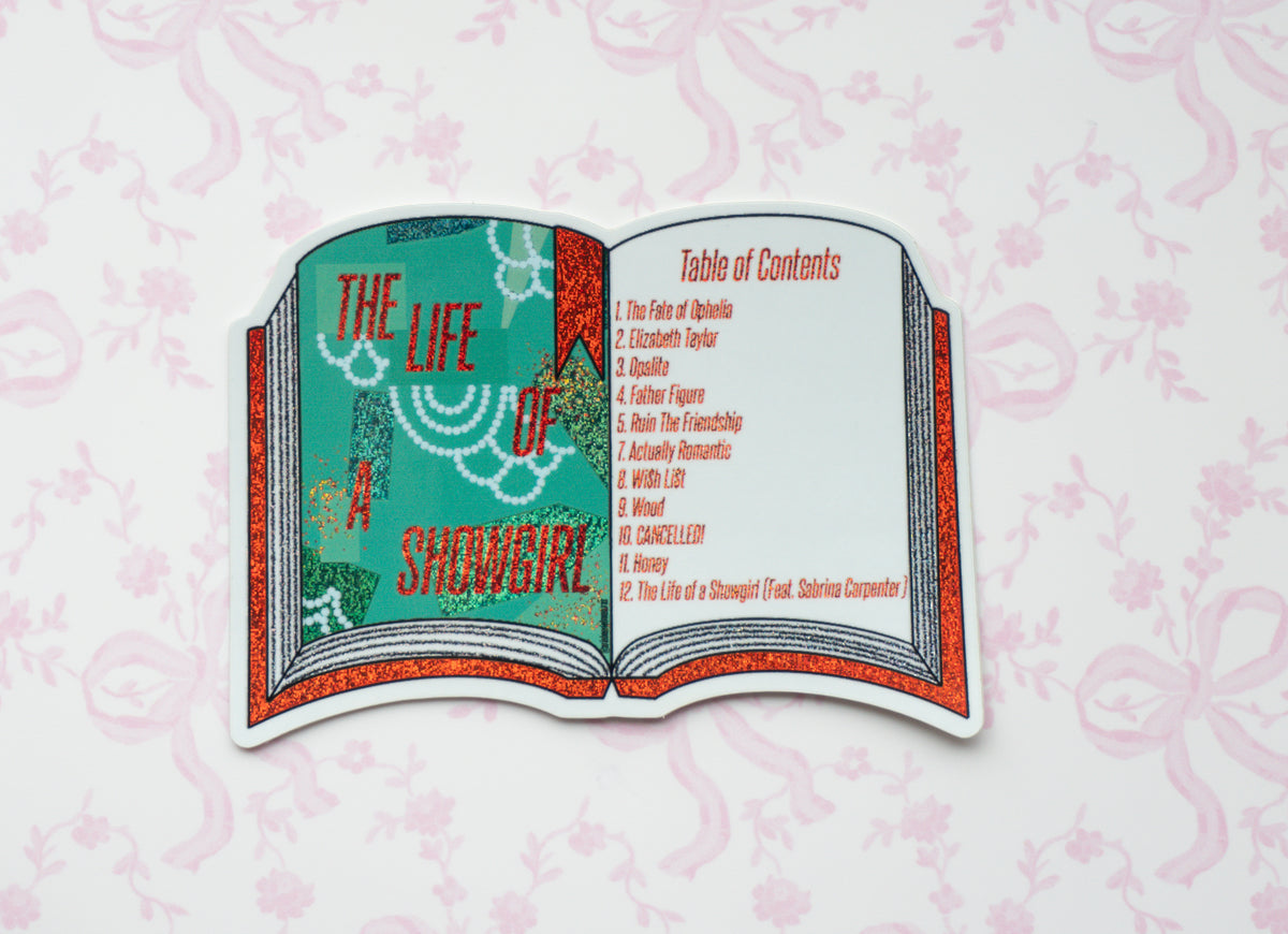 A die-cut sticker shaped like an open book featuring the title 'The Life of a Showgirl' on the left page and a 'Table of Contents' on the right page, styled with a glittery red and teal design, displayed on a light pink patterned background.