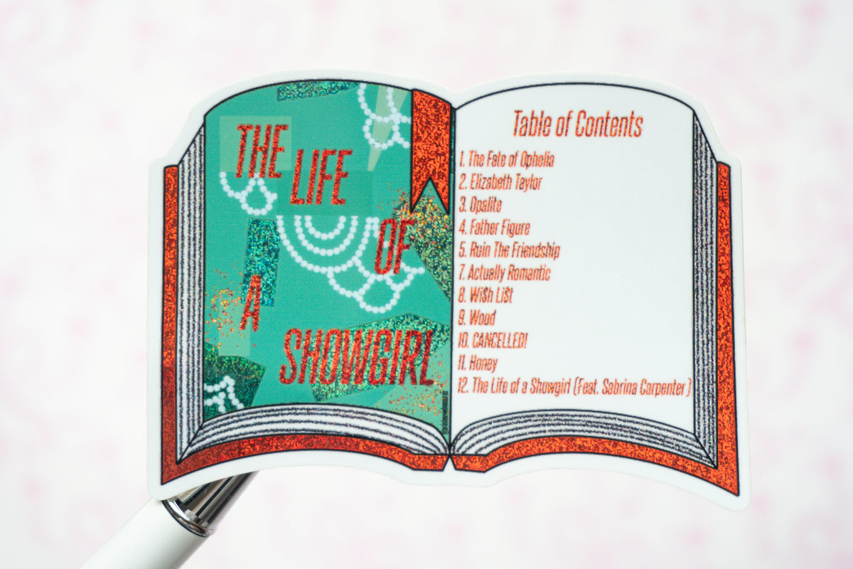 A close-up of an open book-shaped sticker or decal showing the cover art and table of contents for 'The Life of a Showgirl' on a pale pink background.