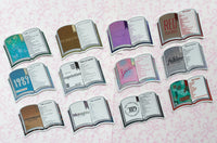 Twelve book-shaped stickers arranged in a grid on a pale pink patterned background. Each sticker depicts an open book with different illustrated covers and titles, including 'RED', '1987', 'reputation', 'folklore', 'Midnights', and others.