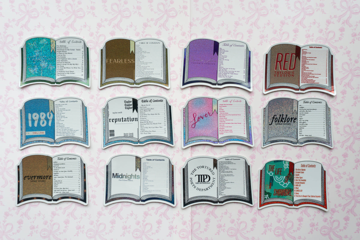 A set of 12 book-shaped stickers arranged in three rows on a light pink patterned background. The stickers depict various classic and popular books with colorful covers, including '1989', 'Reputation', 'lover', 'folklore', 'Evermore', 'Midnights', 'The Third Floor', 'Midnight', 'The Power', 'The Road', and 'Red'.