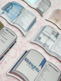 A set of die-cut stickers shaped like open book pages, featuring vintage sci-fi book covers with titles such as 'Midnights' and 'reputation', arranged on a light pink floral background.