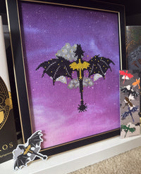 Fourth Wing-inspired cross stitch featuring black dragons, silver clouds, and a golden sword on purple fabric, displayed in a black and gold frame with coordinating dragon stickers.