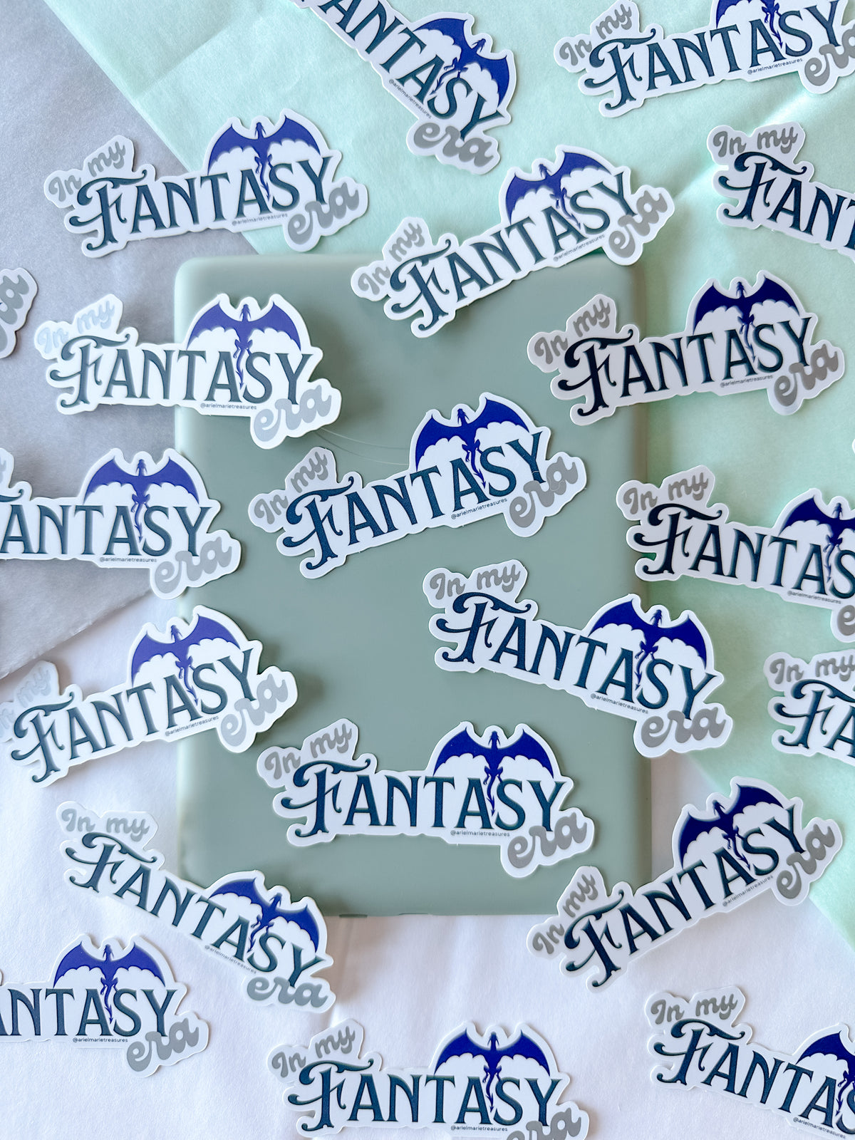 A collection of die-cut stickers featuring the text 'In My Fantasy' in blue script with a blue bat silhouette above, shown scattered on pastel mint and white fabric backgrounds.