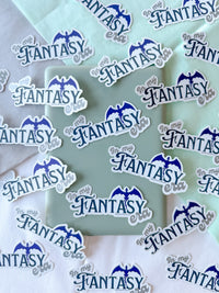 A collection of die-cut stickers featuring the text 'In My Fantasy' in blue script with a blue bat silhouette above, shown scattered on pastel mint and white fabric backgrounds.