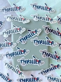 A collection of die-cut stickers featuring the phrase 'In my THRILLER bra' in stylized blue and red lettering with a small hand-drawn camera graphic, arranged on a mint green and white background.