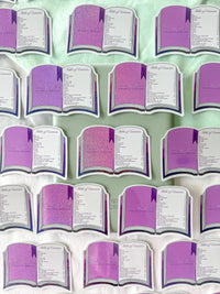 A set of book-shaped stickers arranged on a light mint green fabric background. Each book has purple glittery pages with white borders and printed text, including the heading 'Table of Contents'.