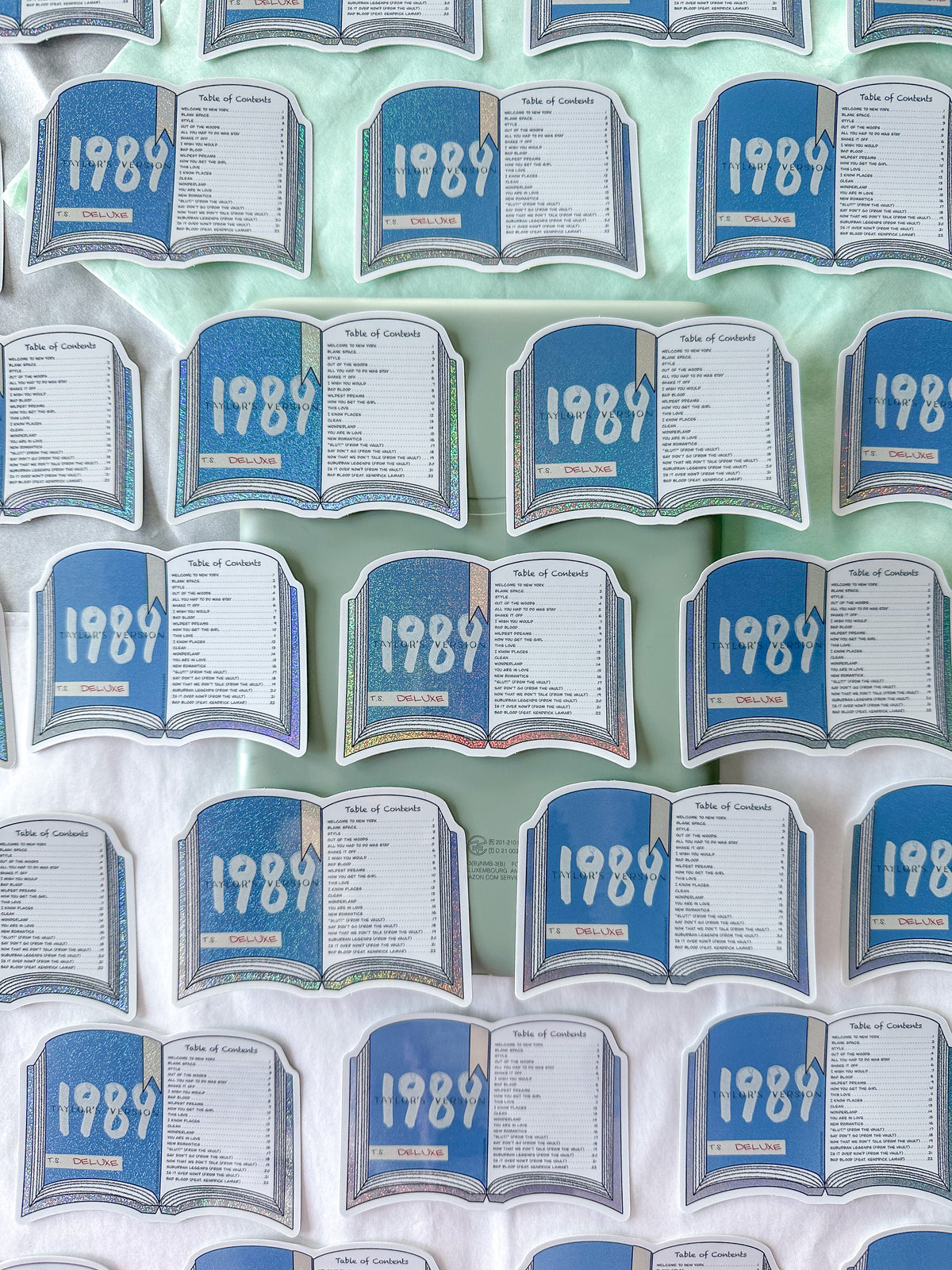 A repeating pattern of small open-book style stickers or labels printed with the year 1989, arranged on a pale mint green surface over a white fabric background.