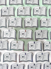 A repeating pattern of novelty pillows shaped like open books, each printed with the text 'The Tortoise and the Hare Department of Psychology' and a circular 'TPD' monogram, arranged on a white and pale green background.